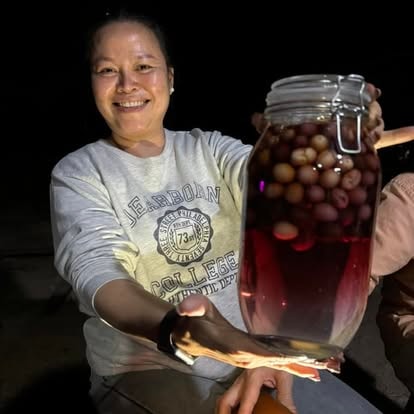 Jiratchaya proudly presenting a large glass jar filled with preserved fruit from the Magic Land — the first product created from the harvest