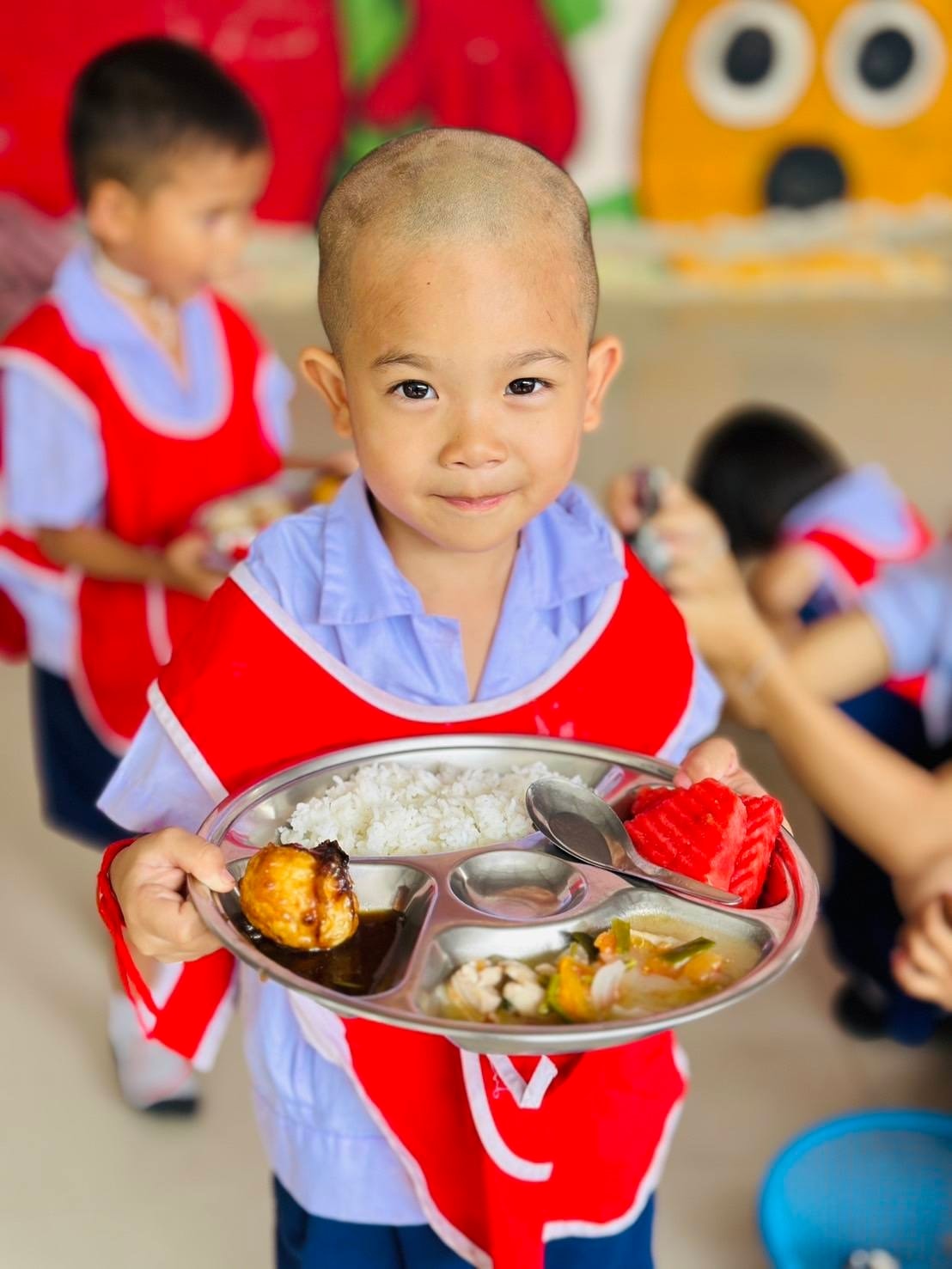 Child holding a tray of prepared food in a colorful classroom